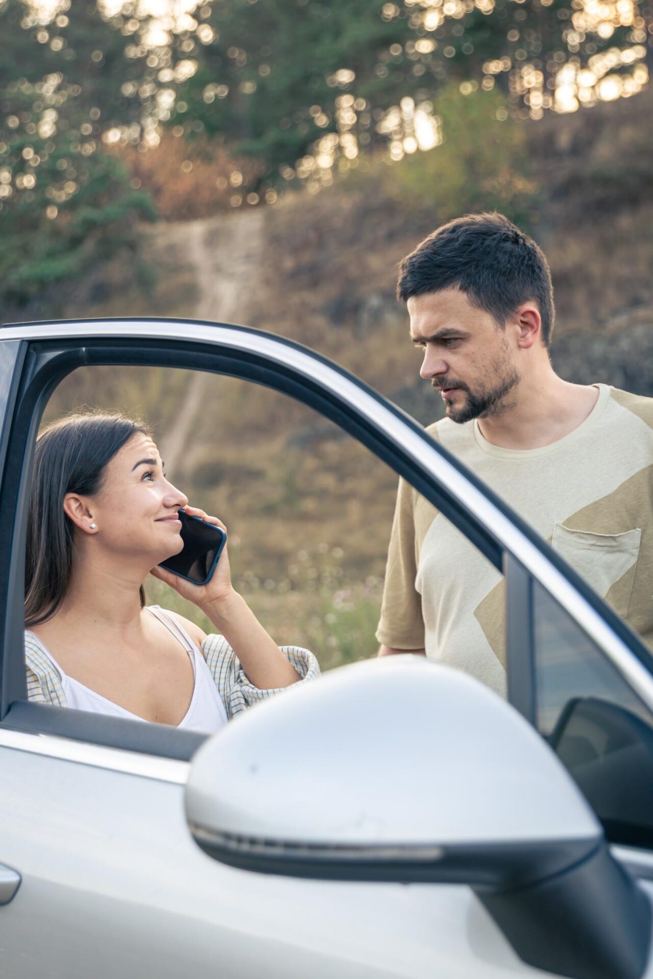 Woman talking on the phone standing near her husband by the car in nature